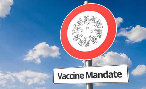 A round street sign for vaccine mandates with a virus within a red circle on a sunny day with cumulous clouds