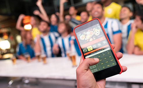 Image of someone sports betting on their cellphone at a crowded bar