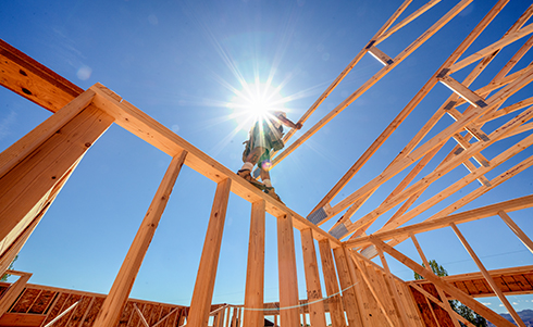 Construction worker standing on the wooden framing of a home while installing roof trussing