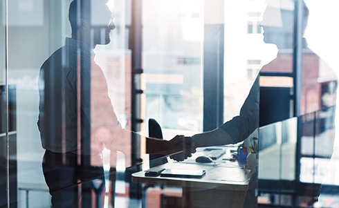 Two people shaking hands in an office behind glass walls