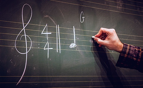 A person writing musical notes on a chalkboard