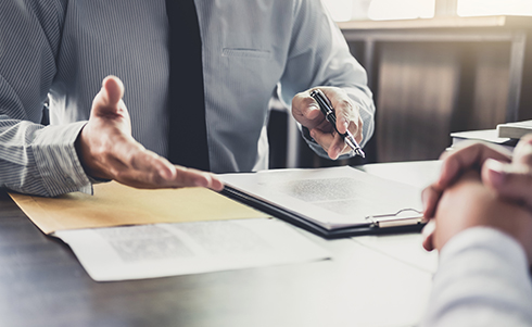 One person gesturing over a contract to another person listening with clasped hands