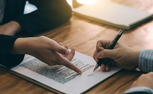 A person pointing to the signature line on a contract for another individual