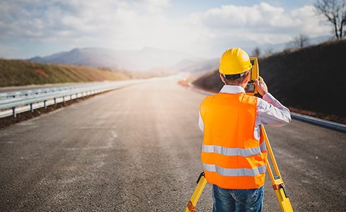 An enginner conducting a survey on a roadway on a sunny day in front of mountains