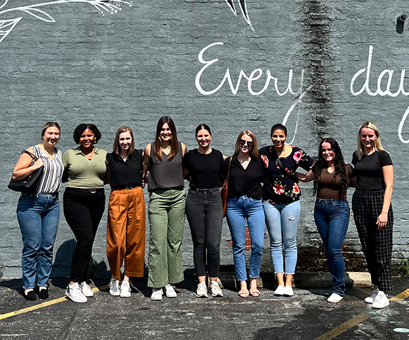 A smiling group of women in front of a wall that says "Every day"