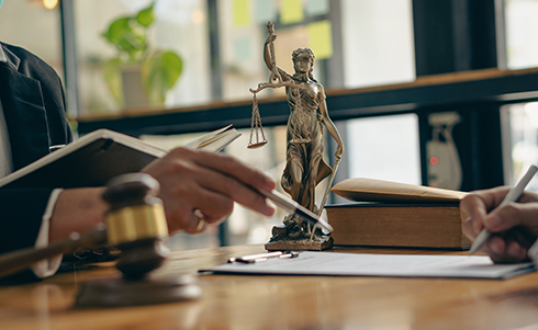 Two individuals reviewing a paper on a table with the scales of justice and a judge's gavel