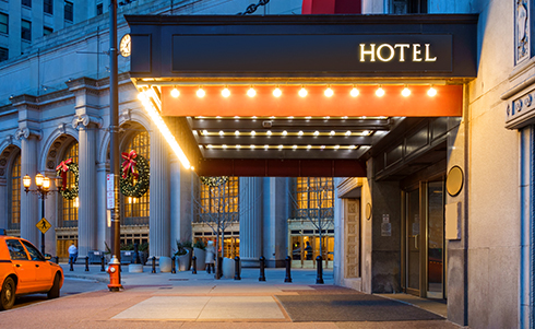 Lit awning outside of a hotel with a taxi cab out front
