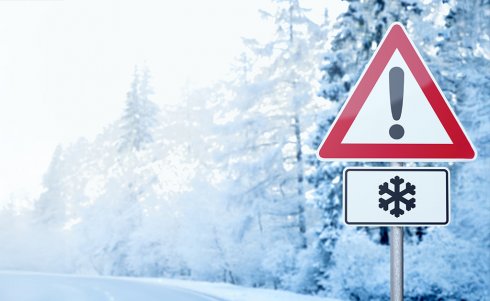 A road sign in the forest on a wintry day with an exclamation mark and snowflake